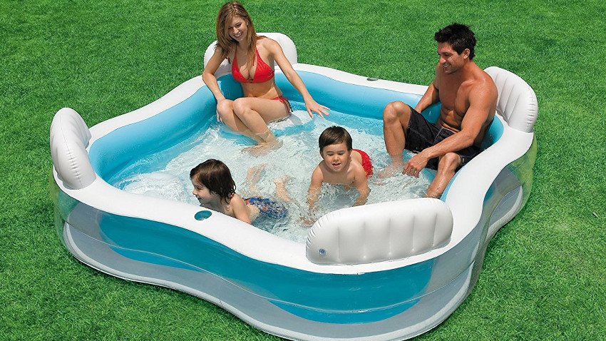 Quadratischer Pool mit Wasser gefüllt. Darin sitzen zwei Erwachsene in der Ecke und zwei Kinder planschen im Wasser