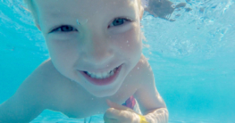 Kind, dass unter Wasser taucht und in eine Kamera lächelt.